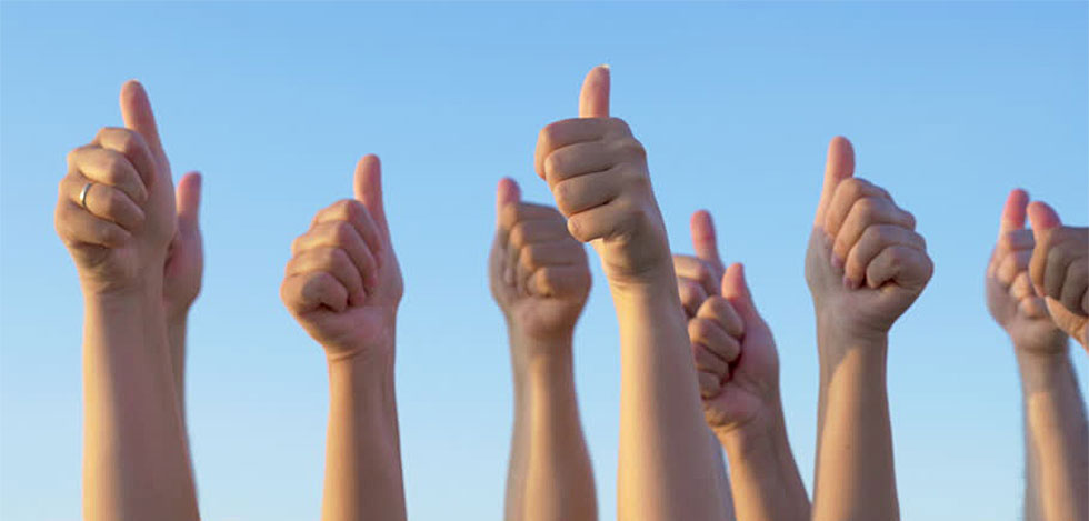 close up of 12 "thumbs up" infront of a clear, blue sky